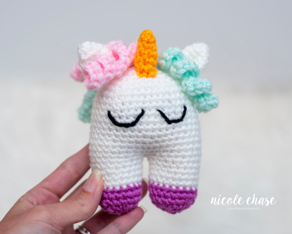 Detail show of the crocheted Elanna the Unicorn baby toy showing the specific stitches for the sleeping eyes and pastel curls. This pattern is designed to be a safe and quick crochet bay toy gift.