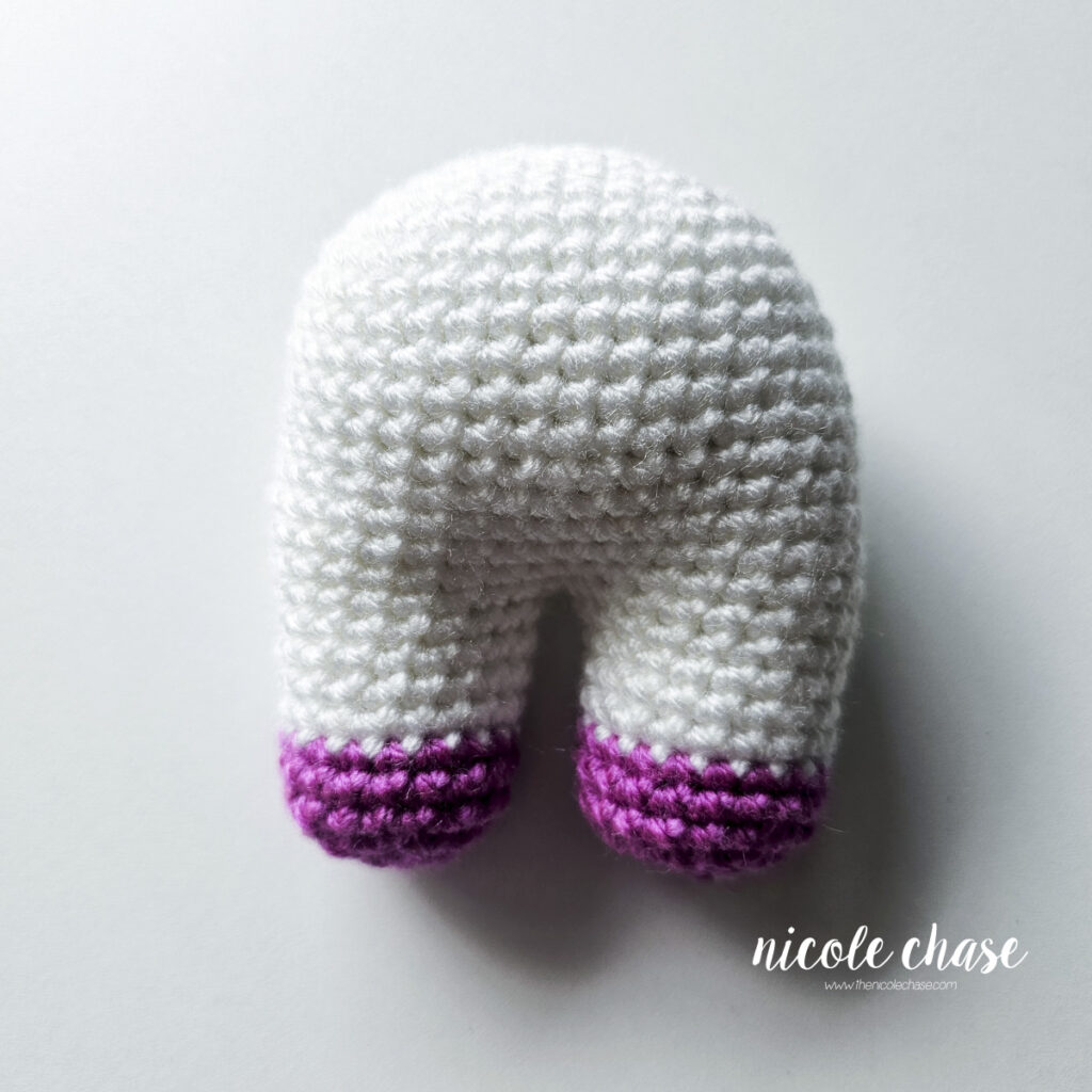 The completed body of the baby unicorn crochet pattern showing the white body with purple hooves at the ends of the legs.