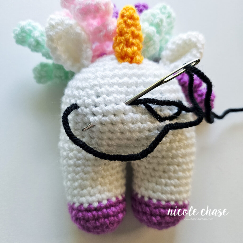 The yarn needle is looping around to create the straight line for the embroidered eye.