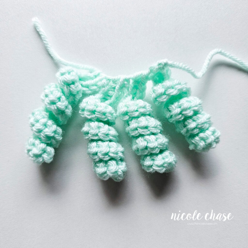 Hair curl A has been completed in a mint yarn with a total of four curls.
