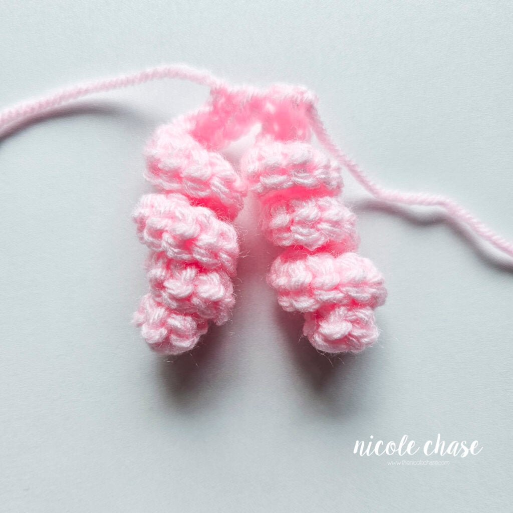 Hair Curl C has been completed in a pink yarn with a total of two curls attached.