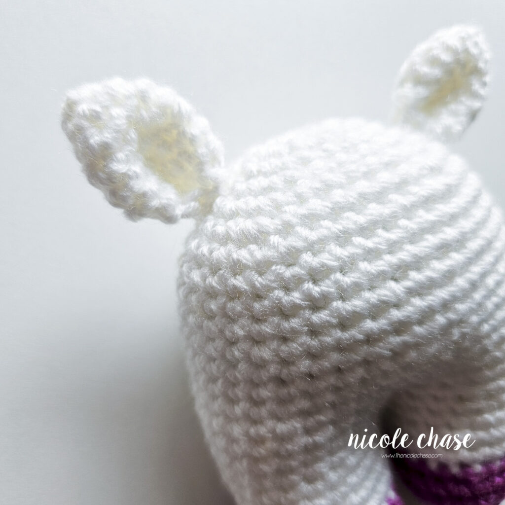 The baby unicorn crochet ears have been sewn into place on top of the head, a close up angled view.