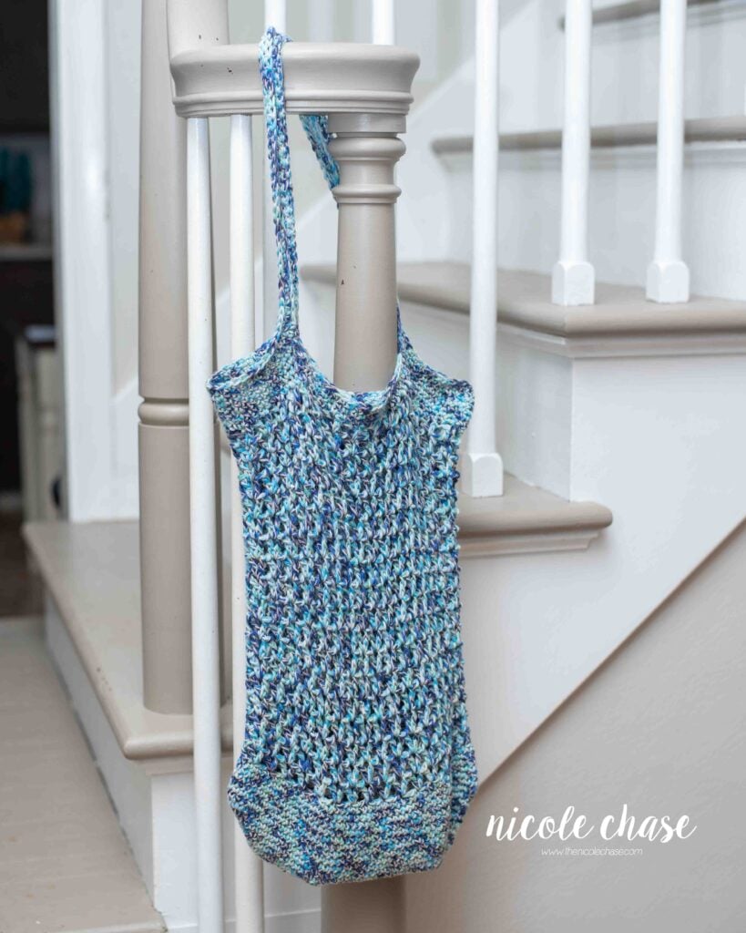 Finished Chase Tote Bag made with this free bag crochet pattern made in blue yarn, hanging on a stair railing.