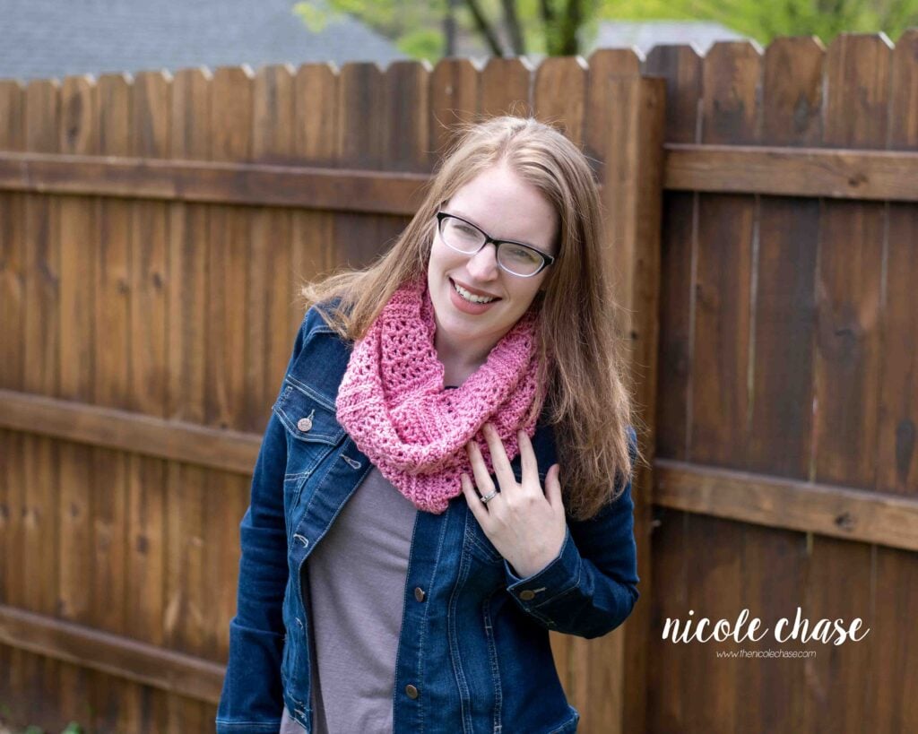 A smiling woman wearing the New Beginnings Cowl in a soft pink yarn, demonstrating the finished free cowl crochet pattern in a new color.