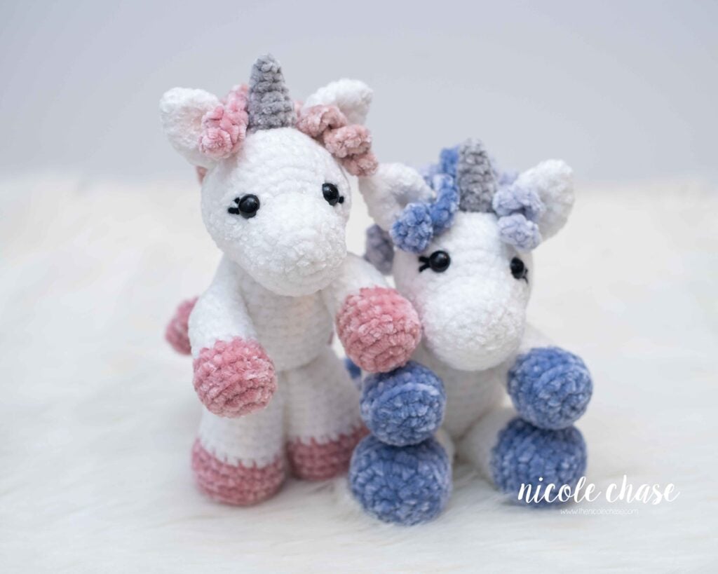 two amigurumi unicorns made in velvet yarn, one white and pink, and one white and blue