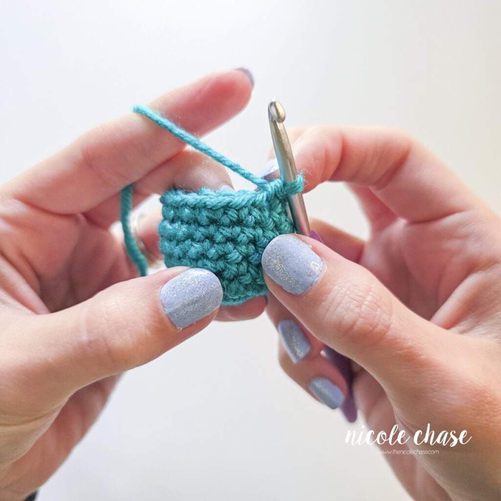 A crochet amigurumi piece shown in teal yarn before any decreasing.