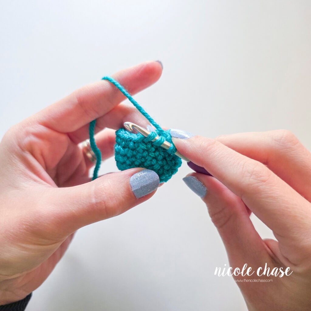 Crochet hook inserted under the front loops of two adjacent single crochet stitches for an invisible decrease.
