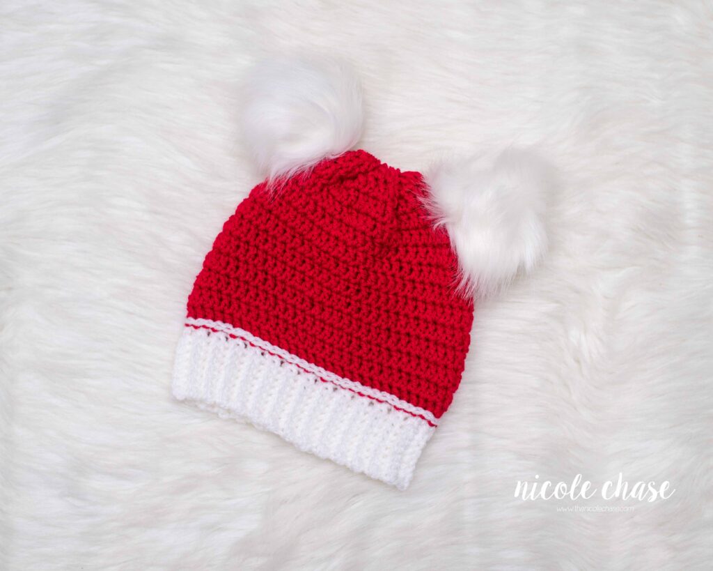red crochet Christmas hat with white brim and two white fur poms