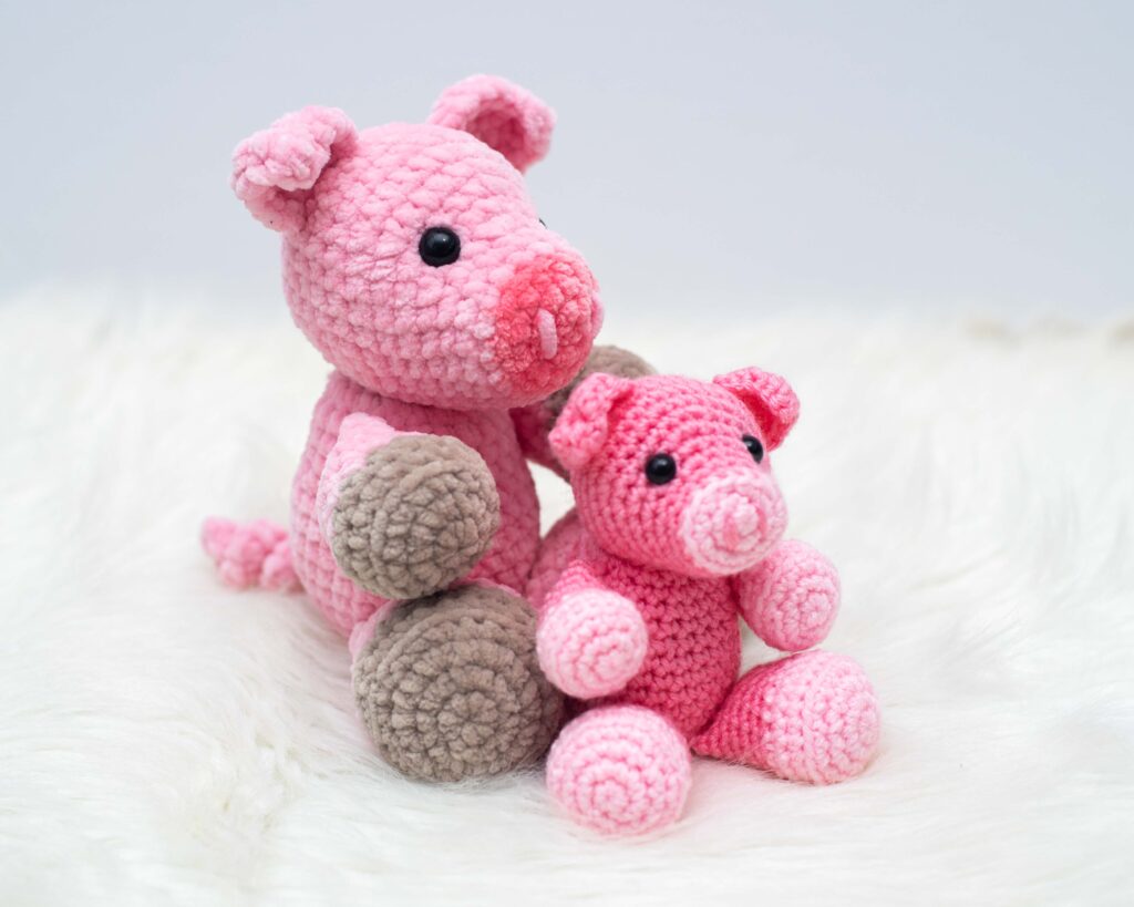 pig crochet pattern in chunky pink and brown yarn next to a smaller pig in pink worsted weight yarn