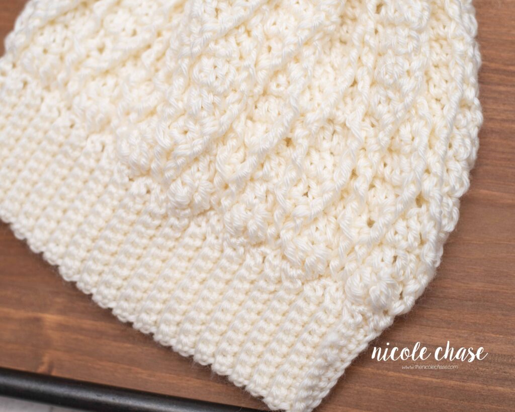 close up view of neutral cream colored cable hat pattern