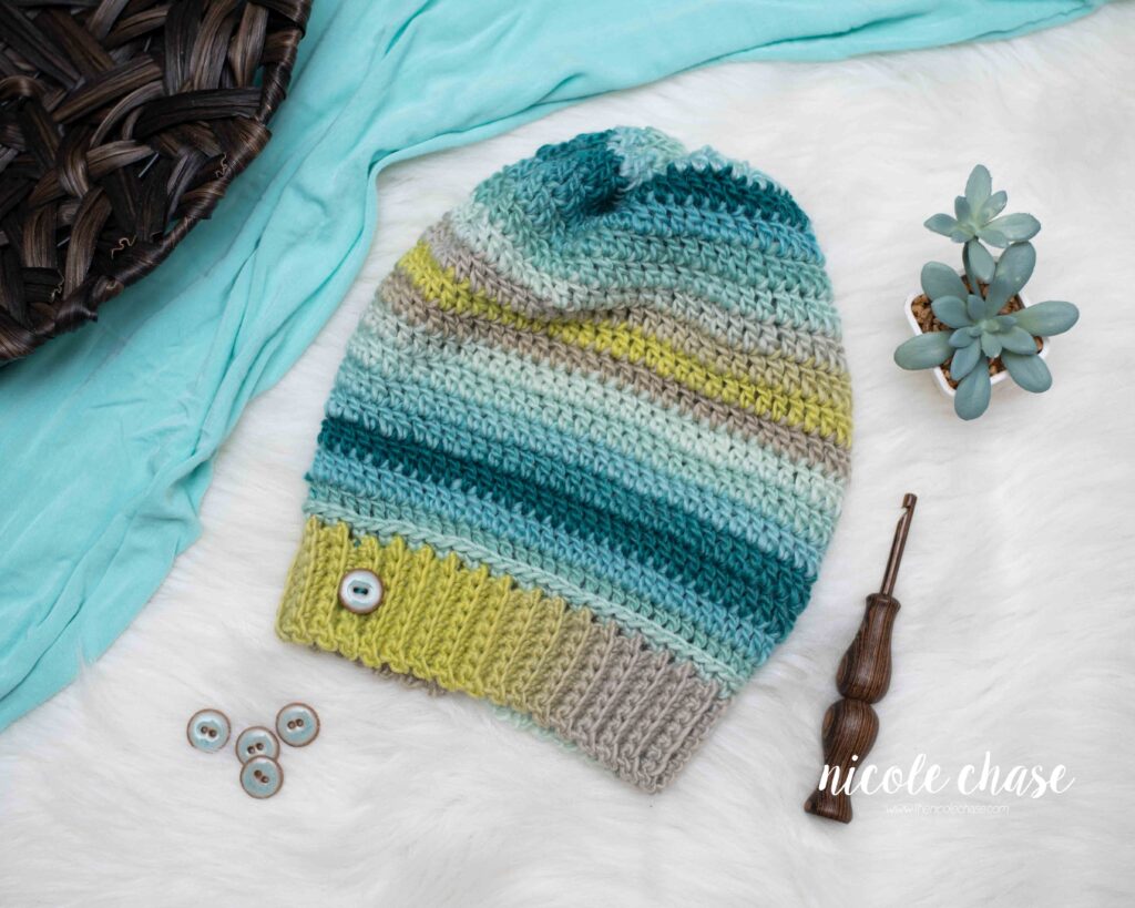 adult slouch beanie crochet pattern shown in a variegated blue and green yarn with blue button on the brim