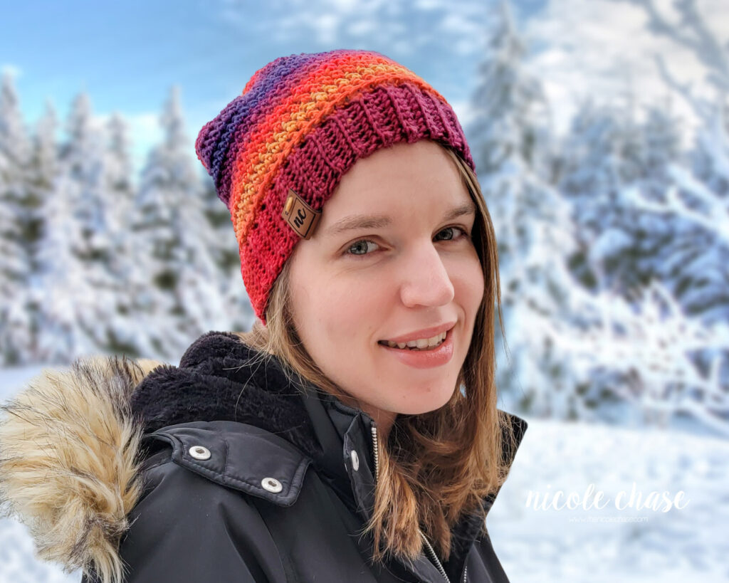 crochet slouch beanie in red, orange, blue, and purple variegated yarn on a smiling woman in a winter scene