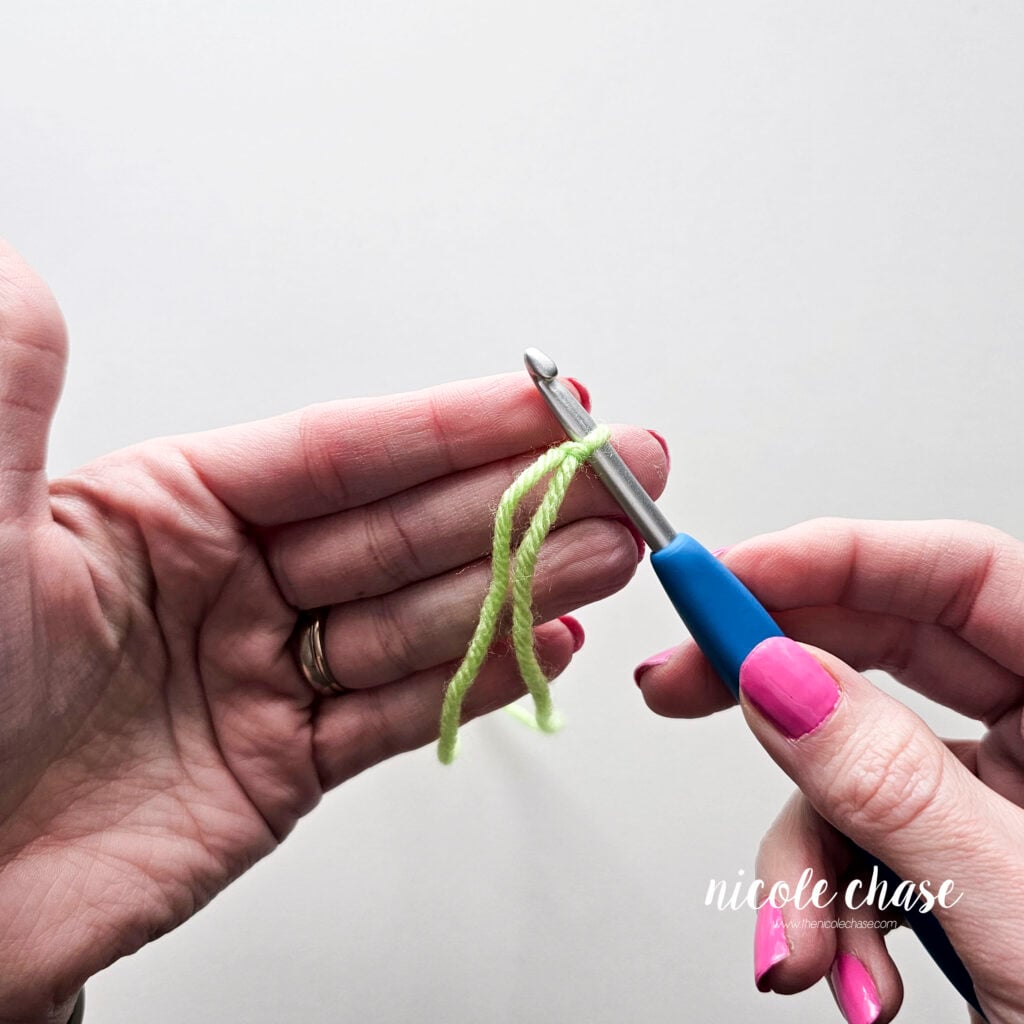 The finished slip knot on the crochet hook with both the working yarn and yarn tail hanging downward.