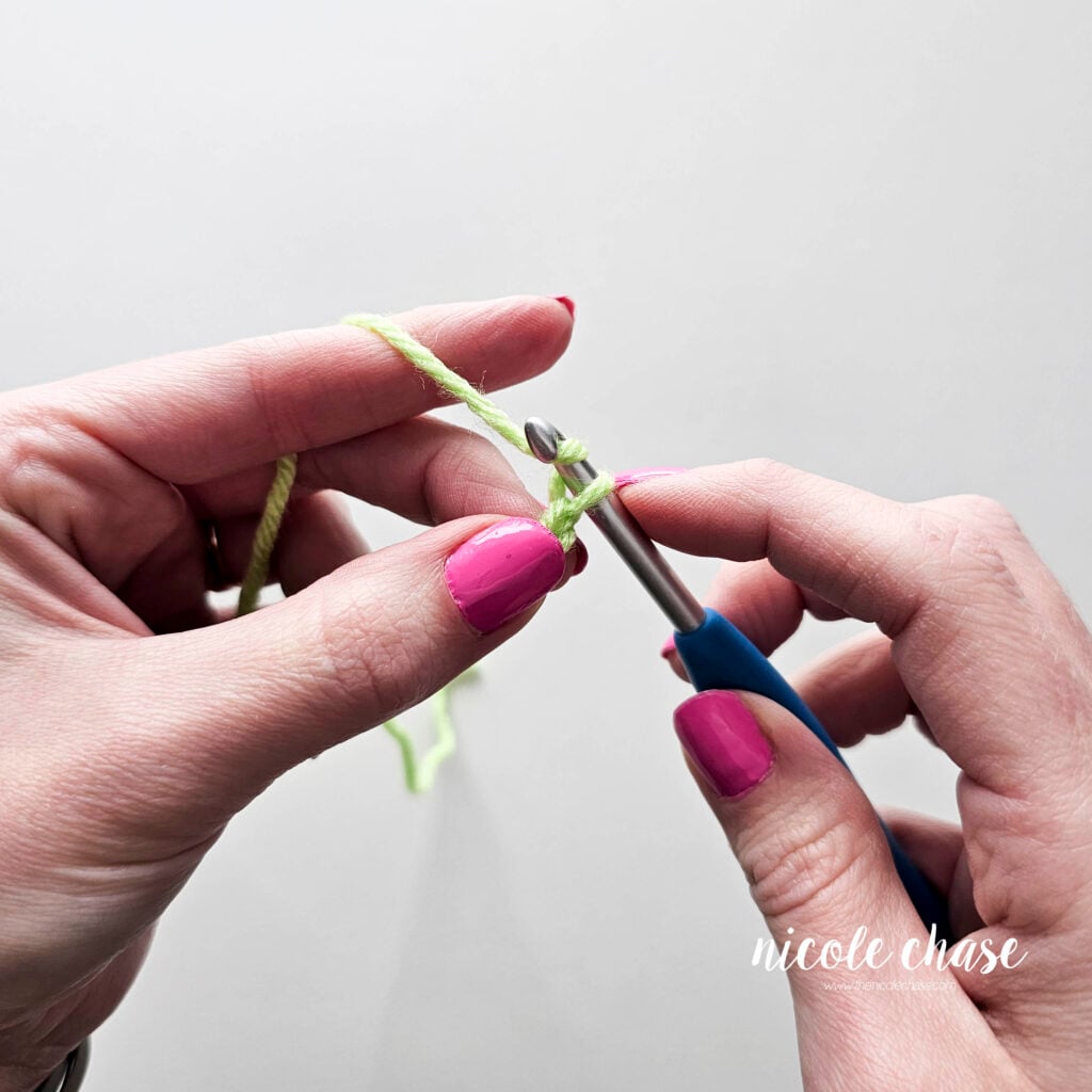 Two chain stitches have been completed and the hook is yarning over to create another.