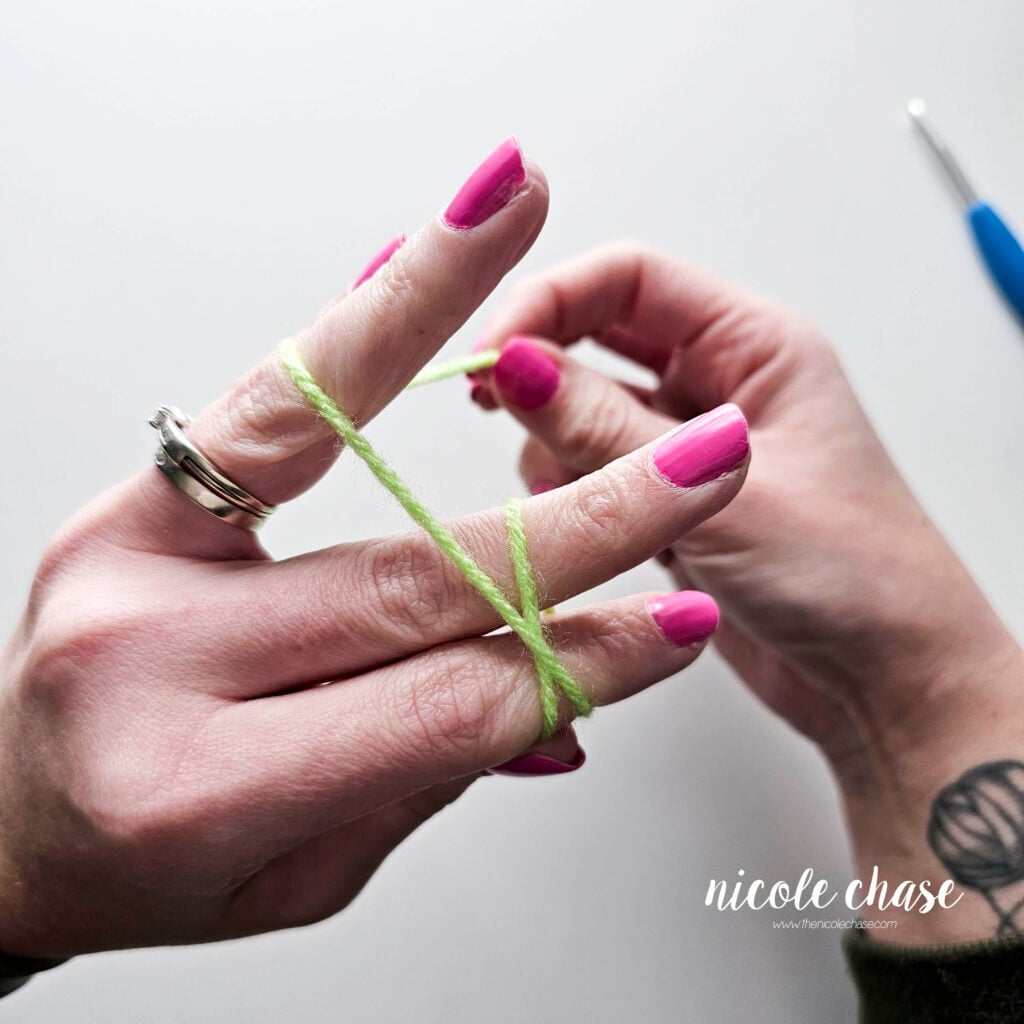 A tutorial image showing the working yarn going between the pinky and ring finger to hold the yarn.