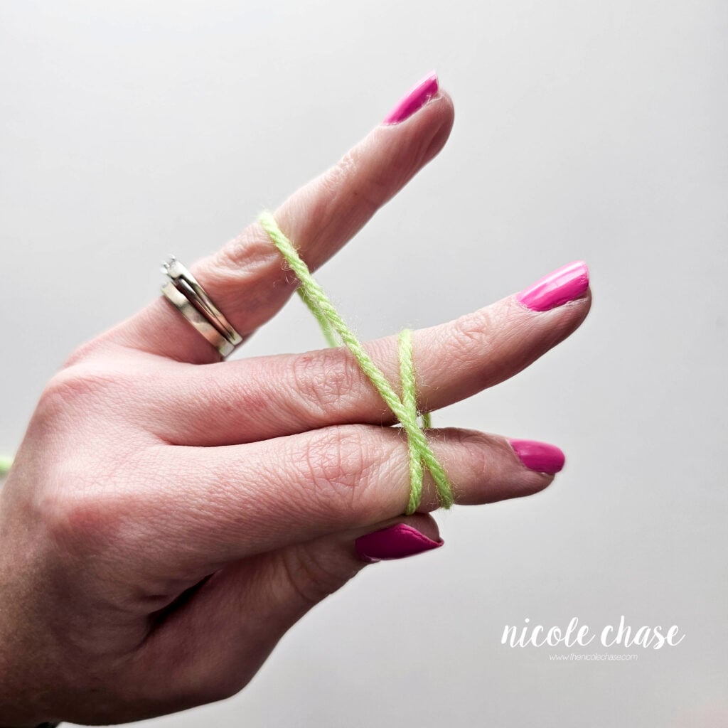 The pinky and ring finger are holding the working yarn and there is an X shape over the pointer and middle fingers for the slip knot tutorial.