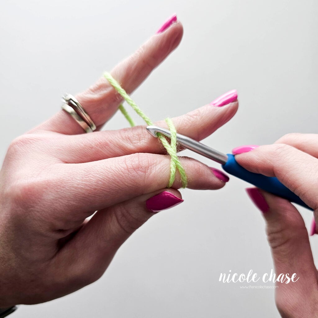Crochet hook is pulling up the back strand of yarn in the process of creating a slip knot.