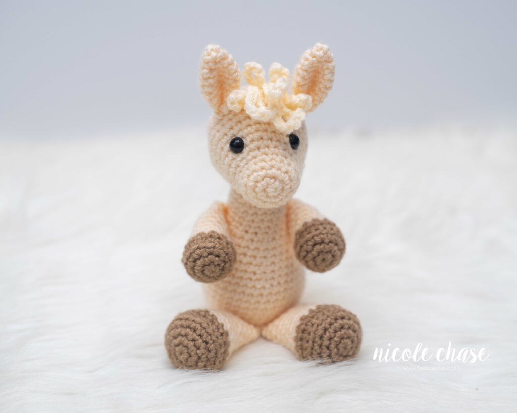 llama crochet pattern in a seated position done in a cream colored yarn with brown colored accents
