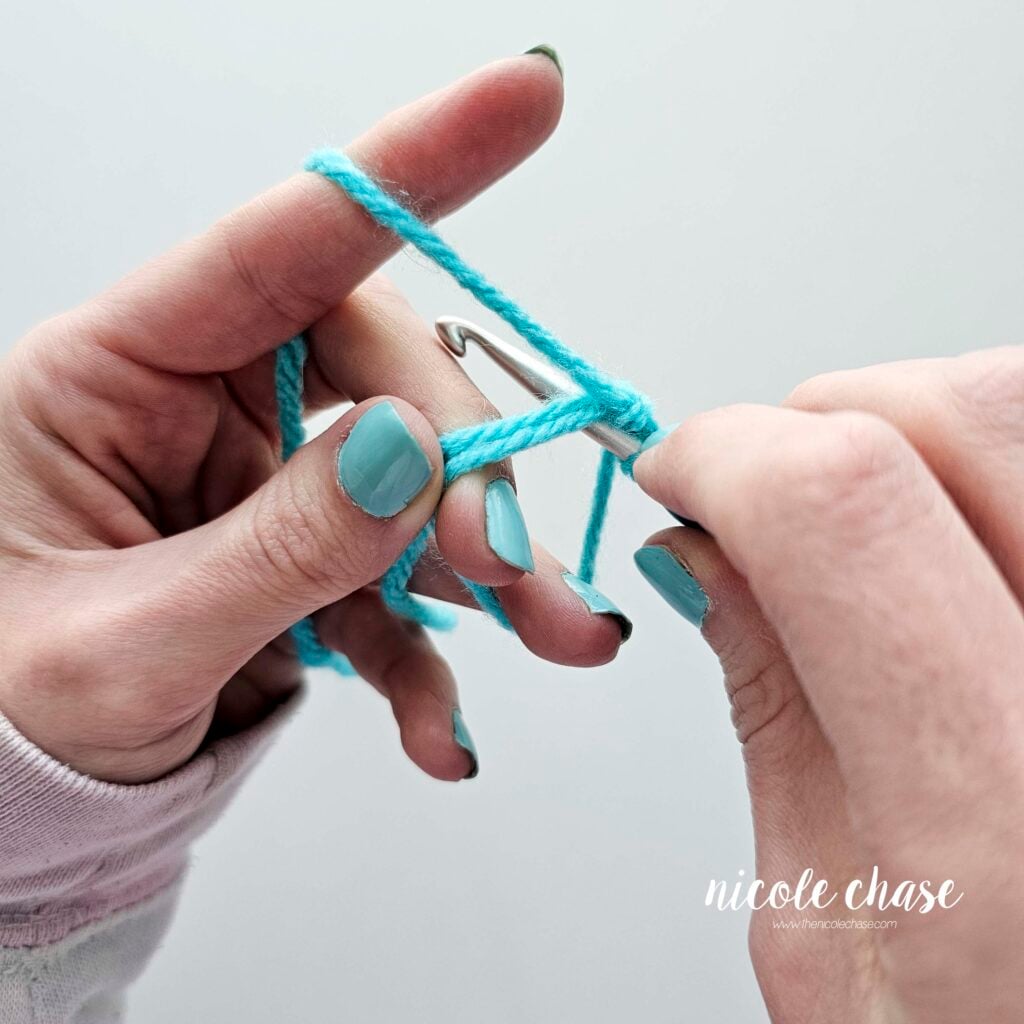 The crochet hook has been inserted into the magic ring, under both strands of yarn.