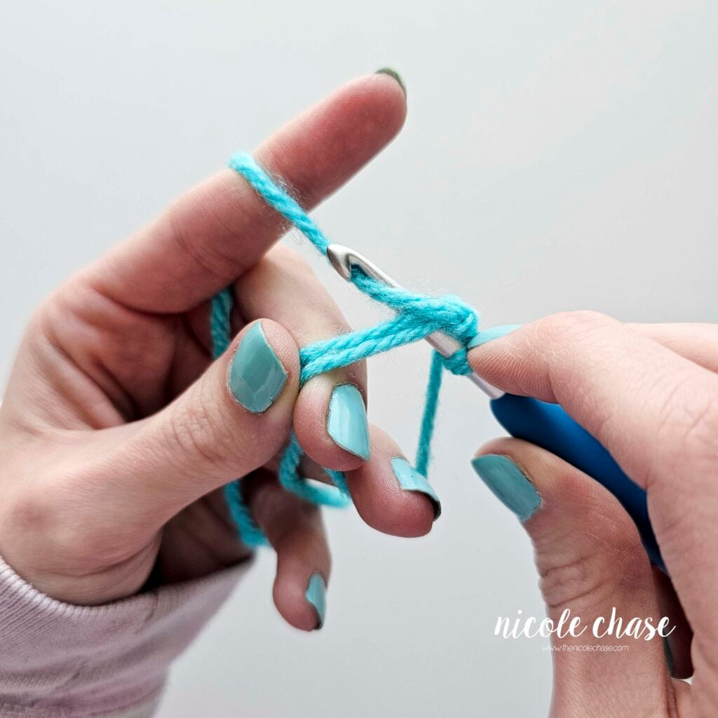 The crochet hook is drawing up a loop of the working yarn through the magic ring.