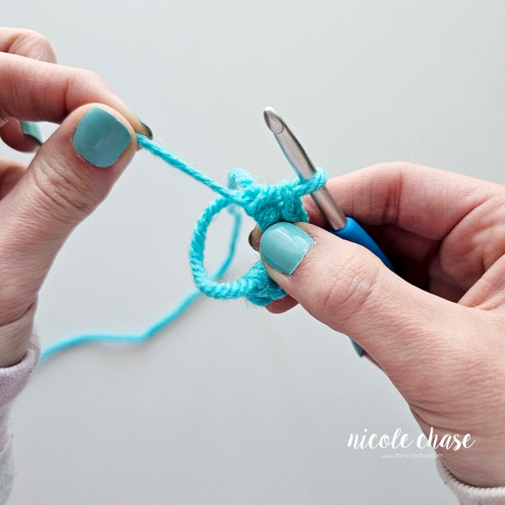 Carefully pulling the yarn tail on the magic ring to close the adjustable loop.
