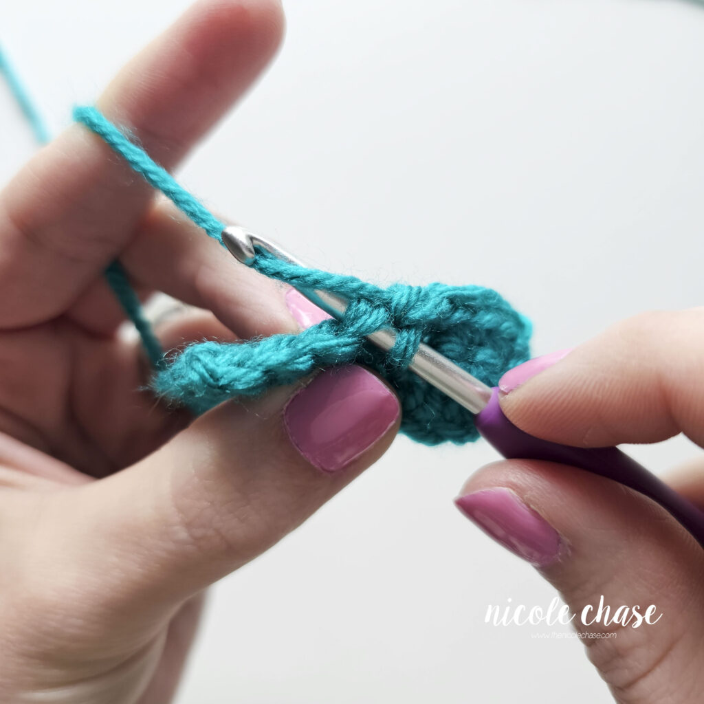Demonstrating the process of working a single crochet stitch into another by inserting your hook and drawing up a loop.