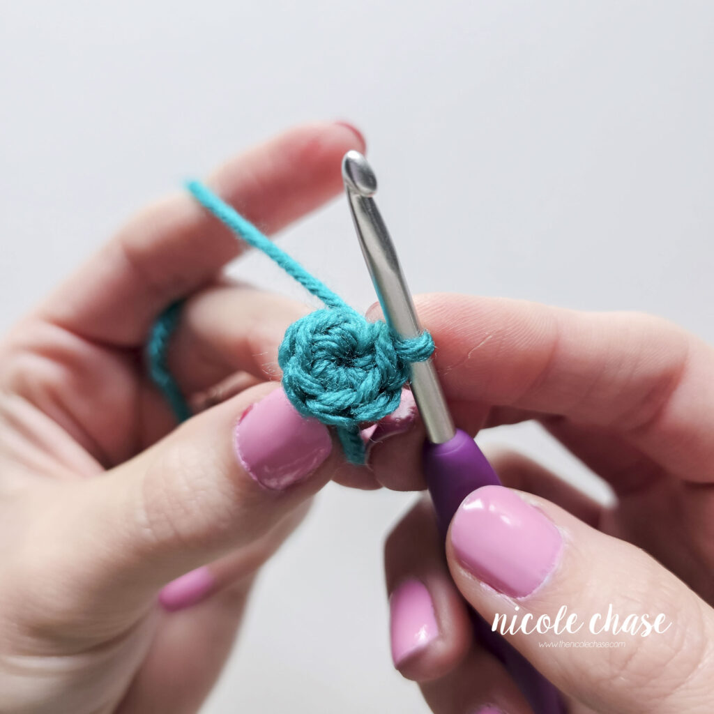 A hand holding a hook and a small circle swatch of single crochet stitches made in a teal yarn.