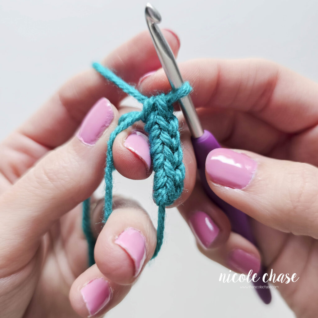 A close up of 6 single crochet stitches worked into a magic ring with teal yarn, prior to the magic ring being closed.