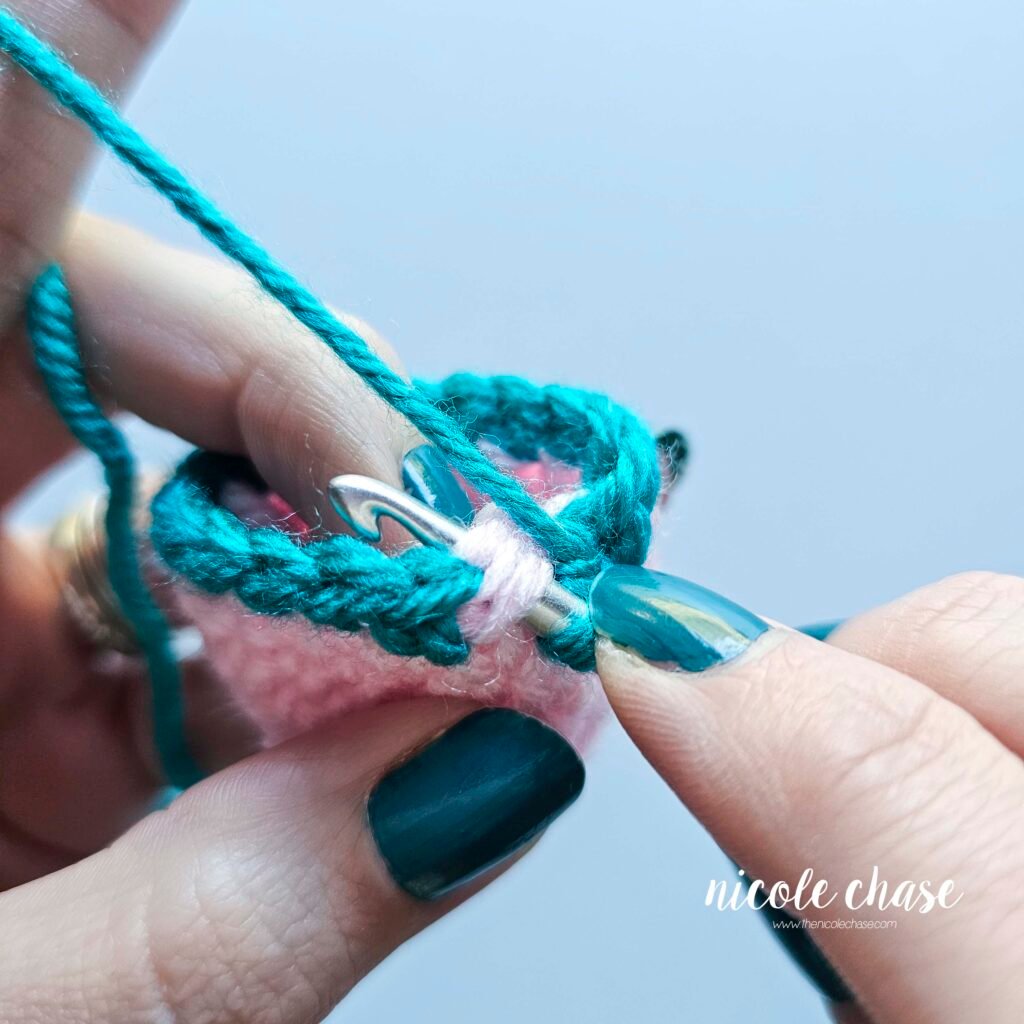 Showing the hook inserted into the unworked front loop and other loops at the invisible color change prior to finalizing the seamless color change.