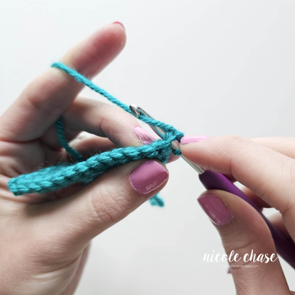 Step-by-step tutorial photo demonstrating catching the yarn to draw up the first loop for a standard decrease stitch.