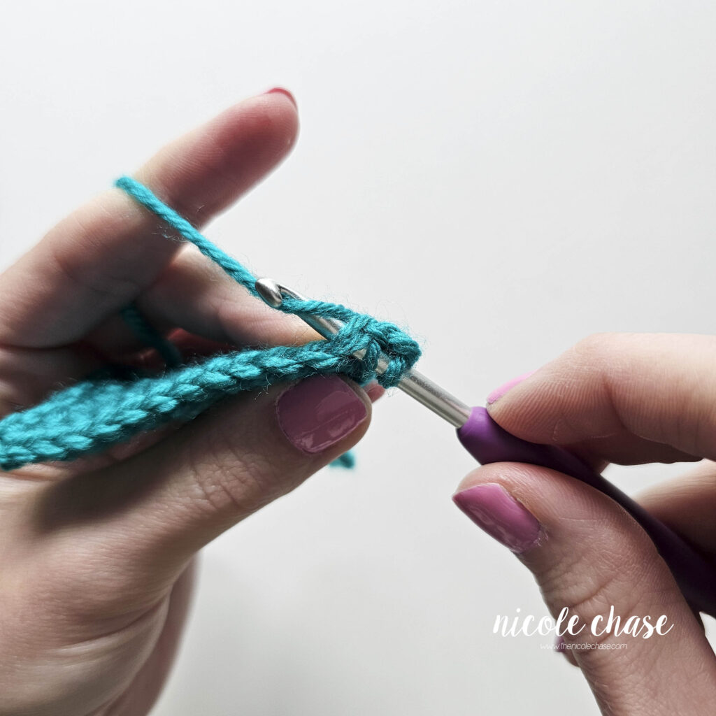 Tutorial image showing the crochet hook catching the working strand to pull up a loop through the second stitch of the sc2tog.