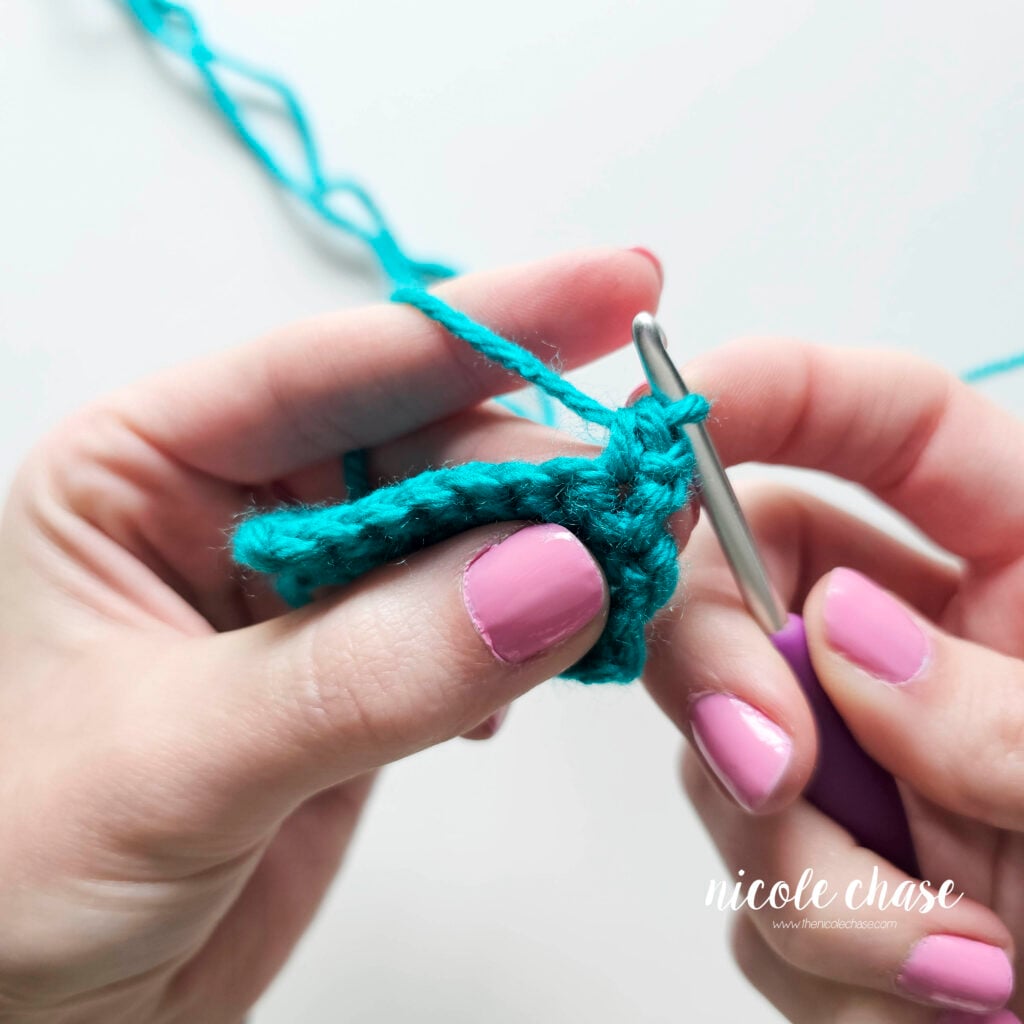 Tutorial photo demonstrating step 1 of a single crochet increase. The image shows the completion of the first regular single crochet stitch in a teal yarn swatch before the second stitch is worked into the same space.