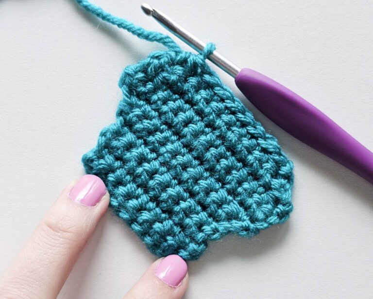 A completed crochet swatch in teal worsted weight acrylic yarn demonstrating fabric shaping. The lower section shows rows widening outward using single crochet increases, while the upper section tapers inward using single crochet decreases (sc2tog). A purple crochet hook rests at the top stitch, and fingers with pink nail polish hold the bottom edge.