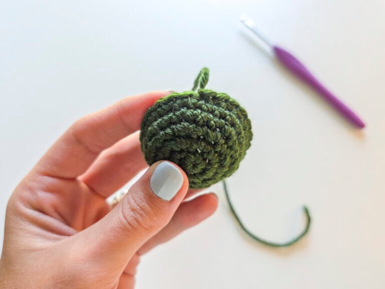 Hand holding a completed green crochet piece that has been joined with a slip stitch and then fastened off.