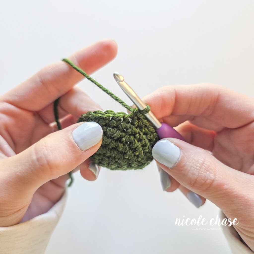 The end of a crochet piece made in green yarn, prior to the final slip stitch and fasten off at the end of the piece.