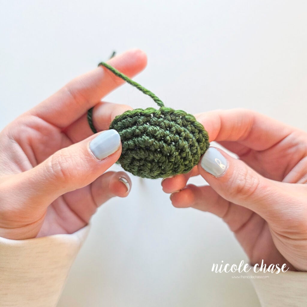 Completed fasten off knot on a green crochet piece, showing a secure yarn tail. 