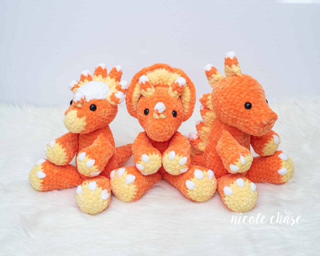 Front view of three candy corn themed crochet plush dinosaurs showing modified candy corn horns and color modifications in orange, yellow, and white chenille plush yarn.