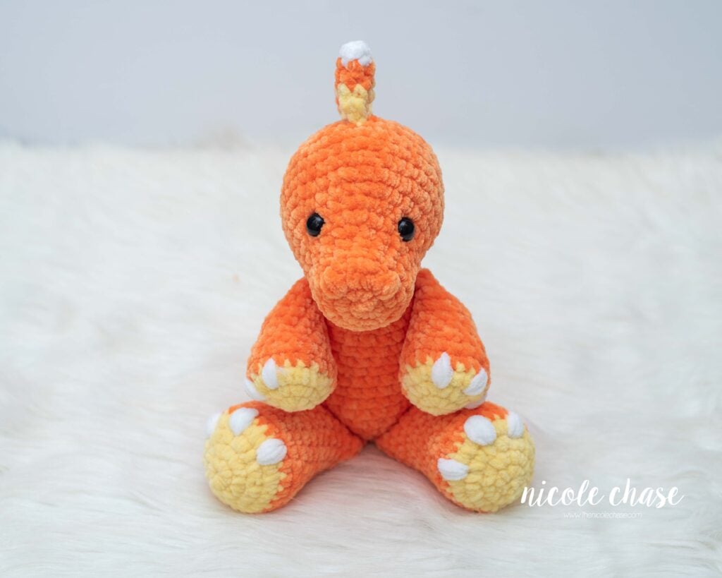 Front view of Mini Toby the Tarbosaurus crocheted in orange plush yarn with yellow feet, featuring candy corn spikes centered on top of the head and down the back.
