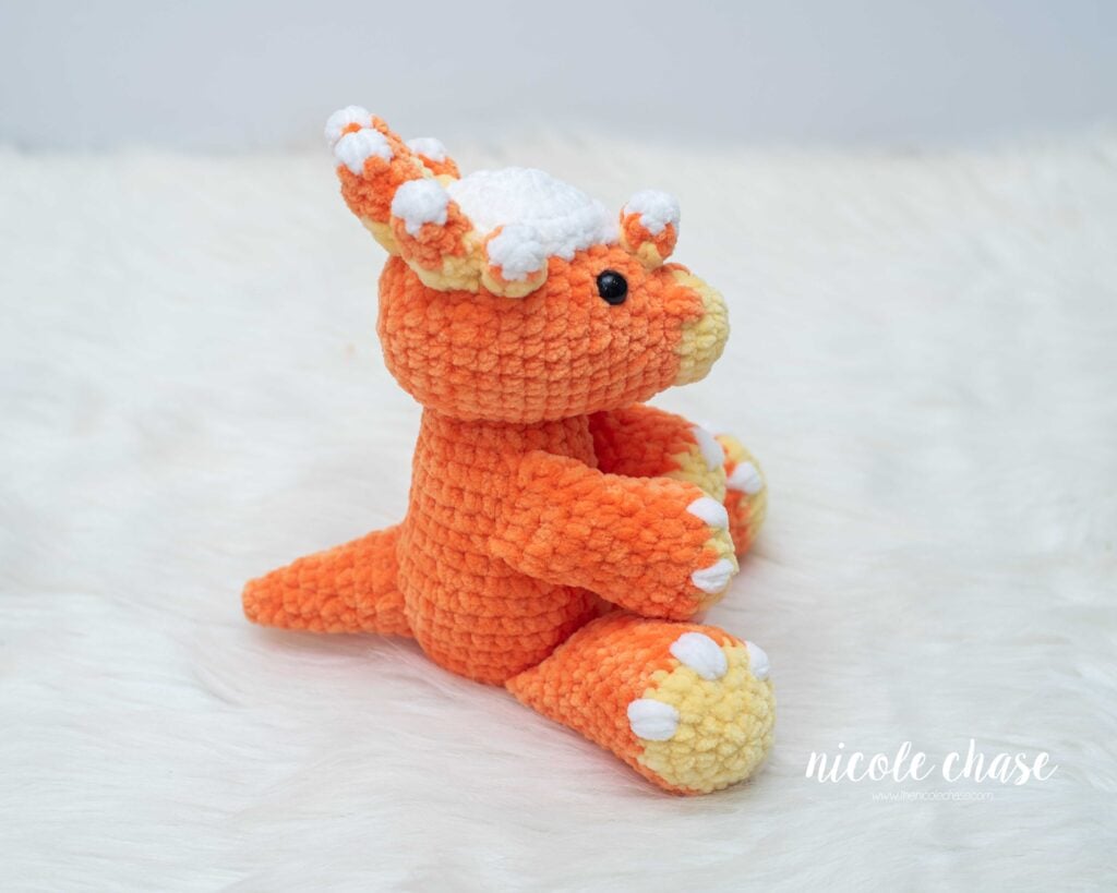 Side profile view of Mini Stevie the Stygimoloch crocheted plush, showing the tail, arm placement, and candy corn horn accents.