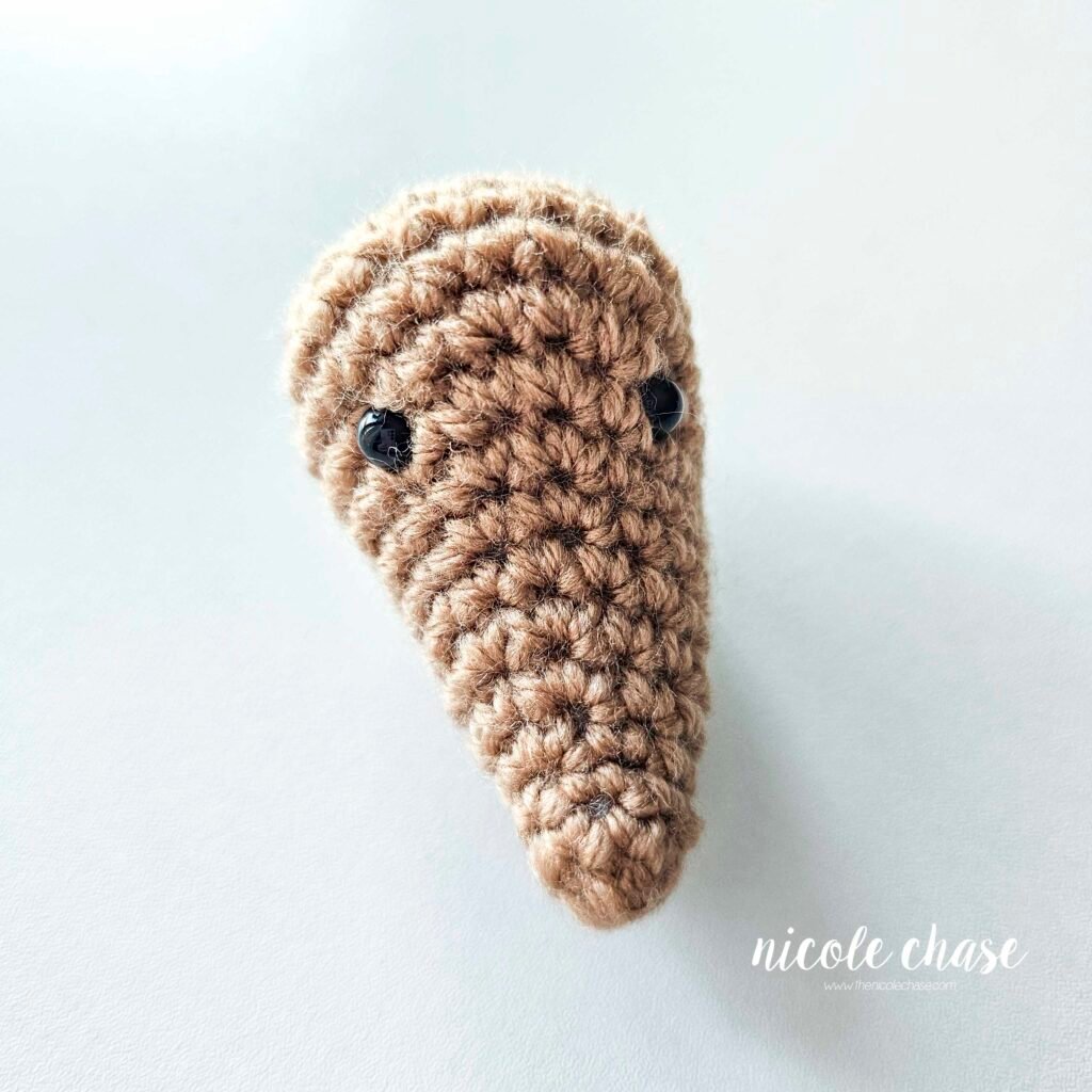 Finished crochet mouse head for the Mavis the Mouse crochet pattern, made in brown yarn with small black safety eyes. 