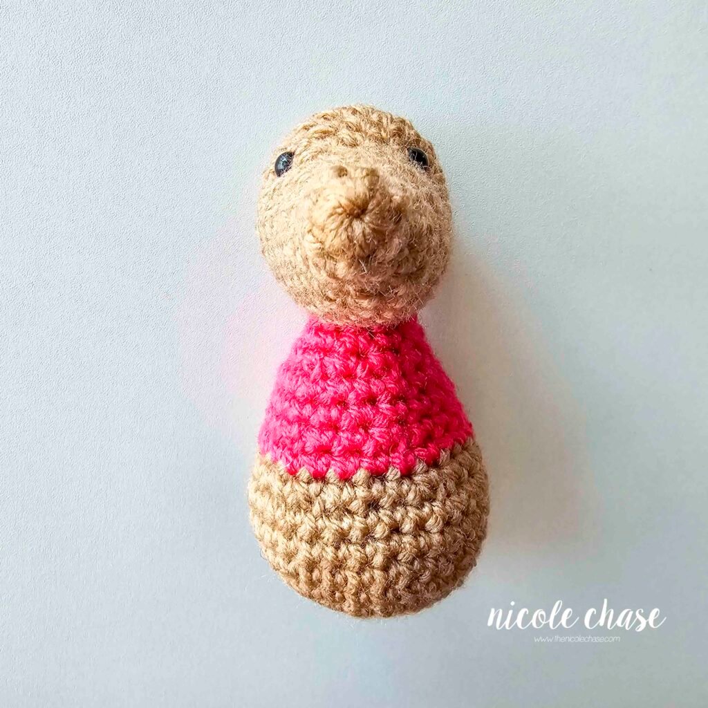 The body of the crochet mouse has been sewn into place on the bottom of the mouse's head, view 1.