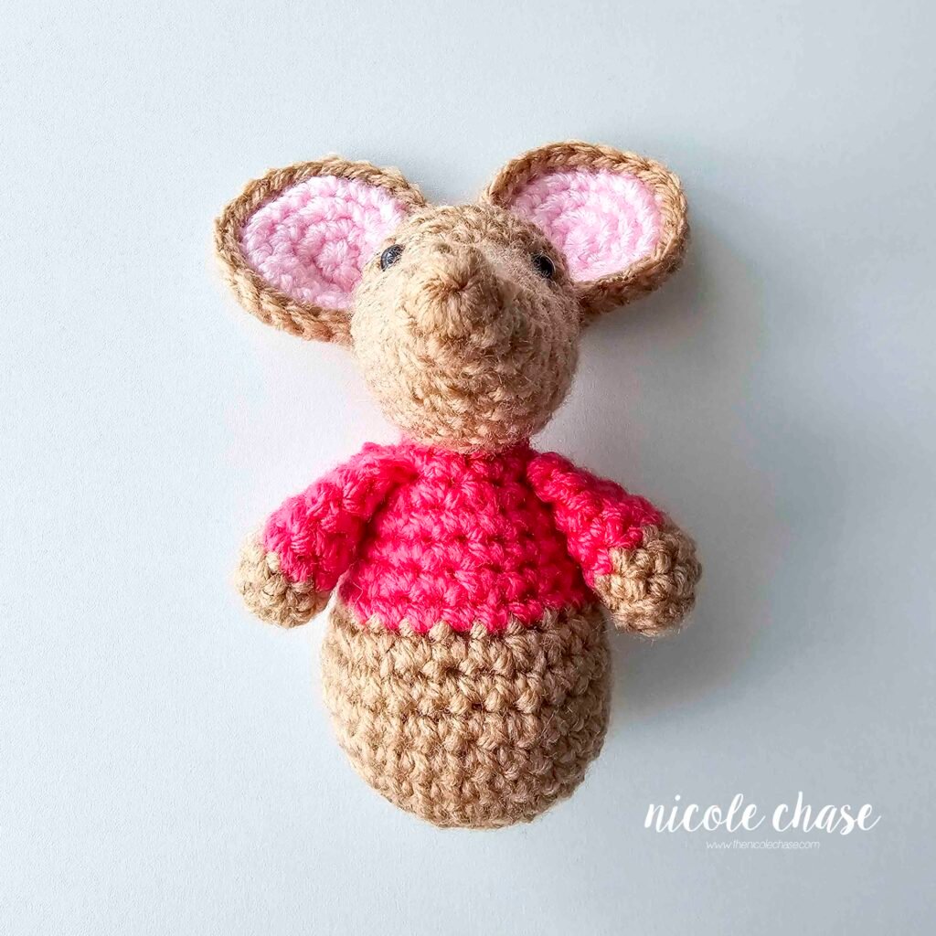 The arms of the crochet mouse have been sewn into place on each side of the body, view 3.
