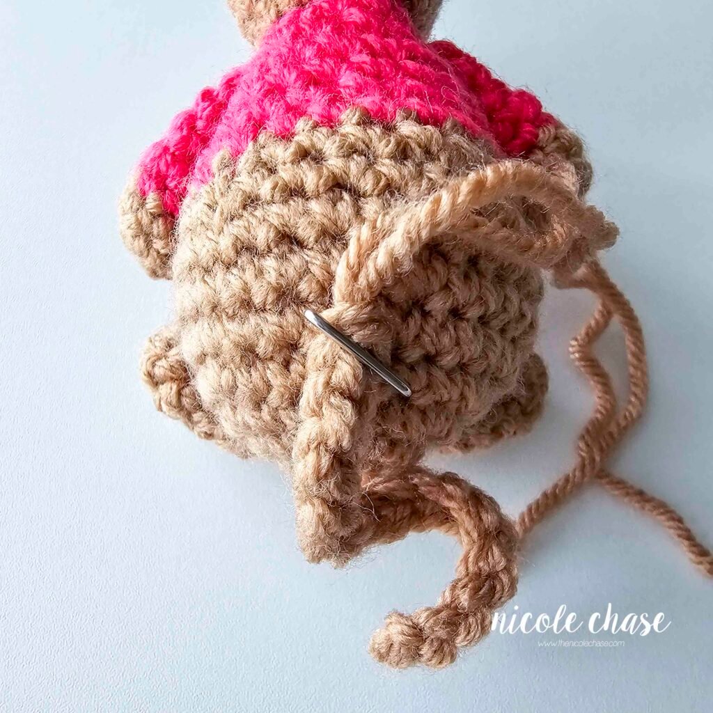 The crochet mouse tail has been pinned into place on the back of the body. 