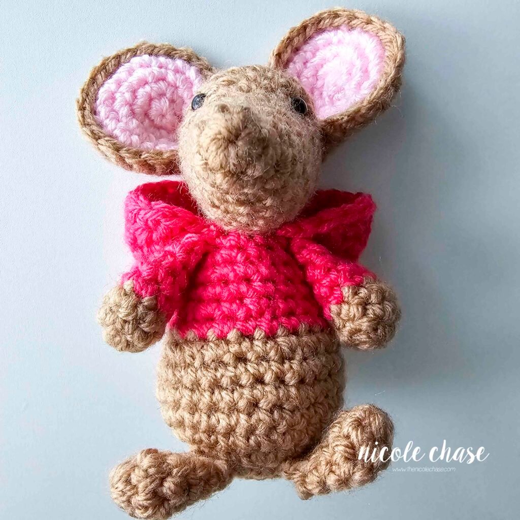 The hood of the crochet mouse's sweatshirt has been sewn into place behind the mouse's head, view 1. 