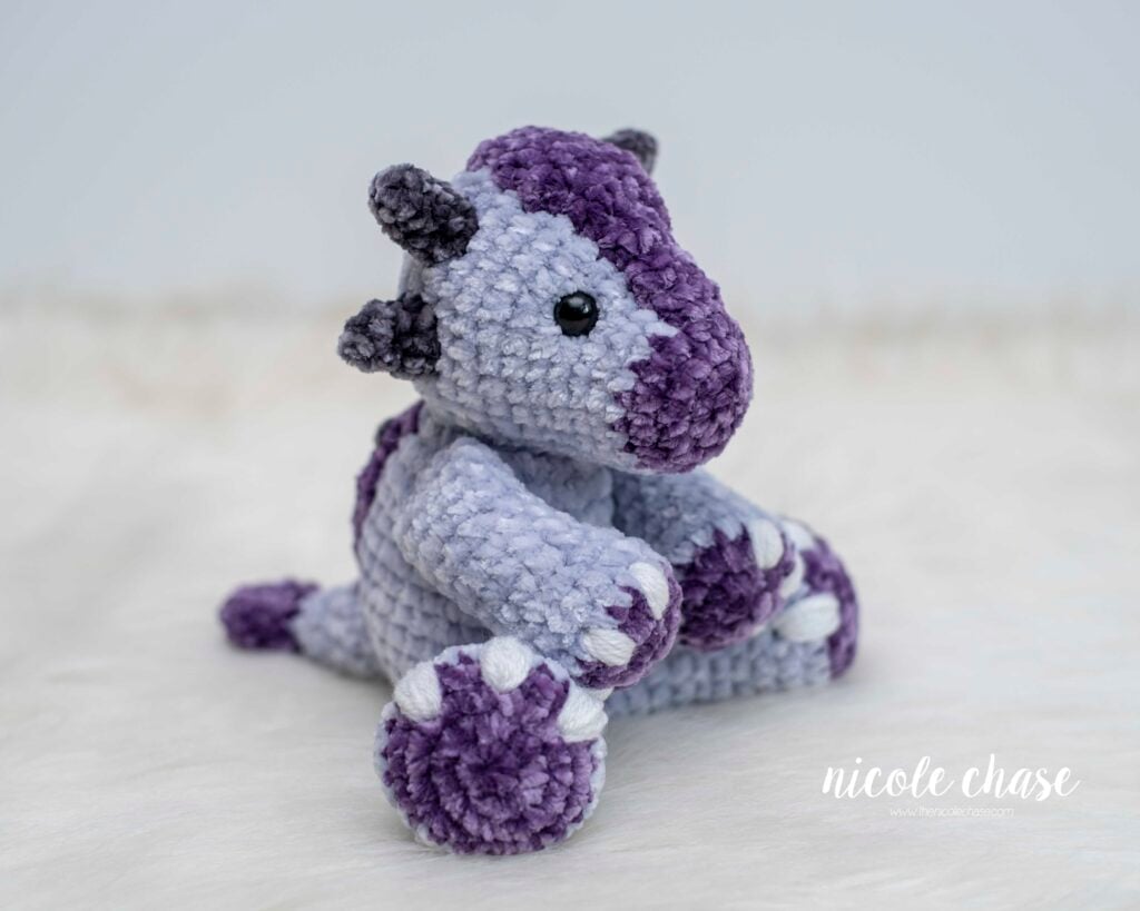 Crochet Mini Archie the Ankylosaurus dinosaur plushie made with light purple and dark purple chenille velvet yarn.