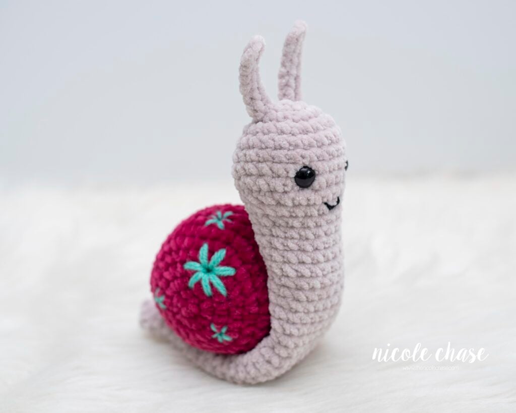 Side view of a free chunky yarn amigurumi snail plushie crocheted in soft plush chenille yarn.
