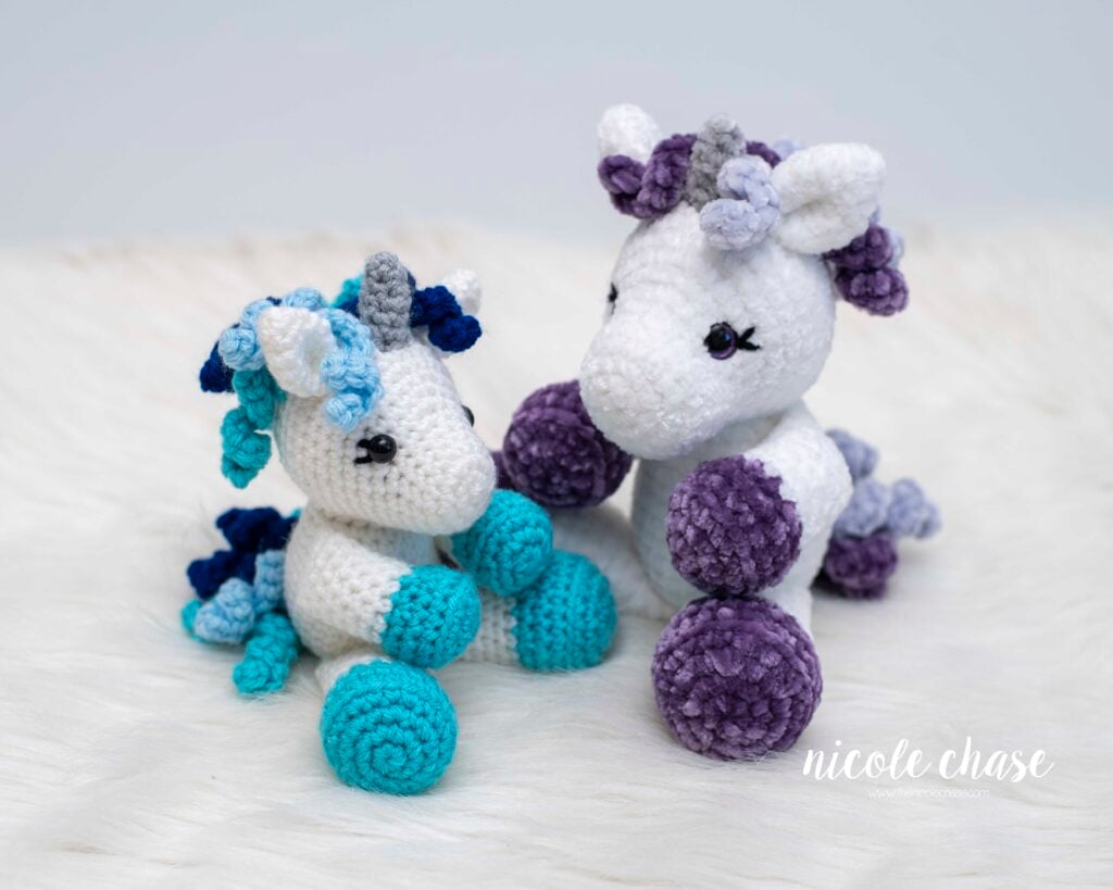 Side-by-side comparison of Mini Poppy the Unicorn crocheted in two different yarn weights: worsted weight yarn (small size) and plush velvet yarn (larger size). This showcases the versatility of this free mini unicorn crochet pattern. 