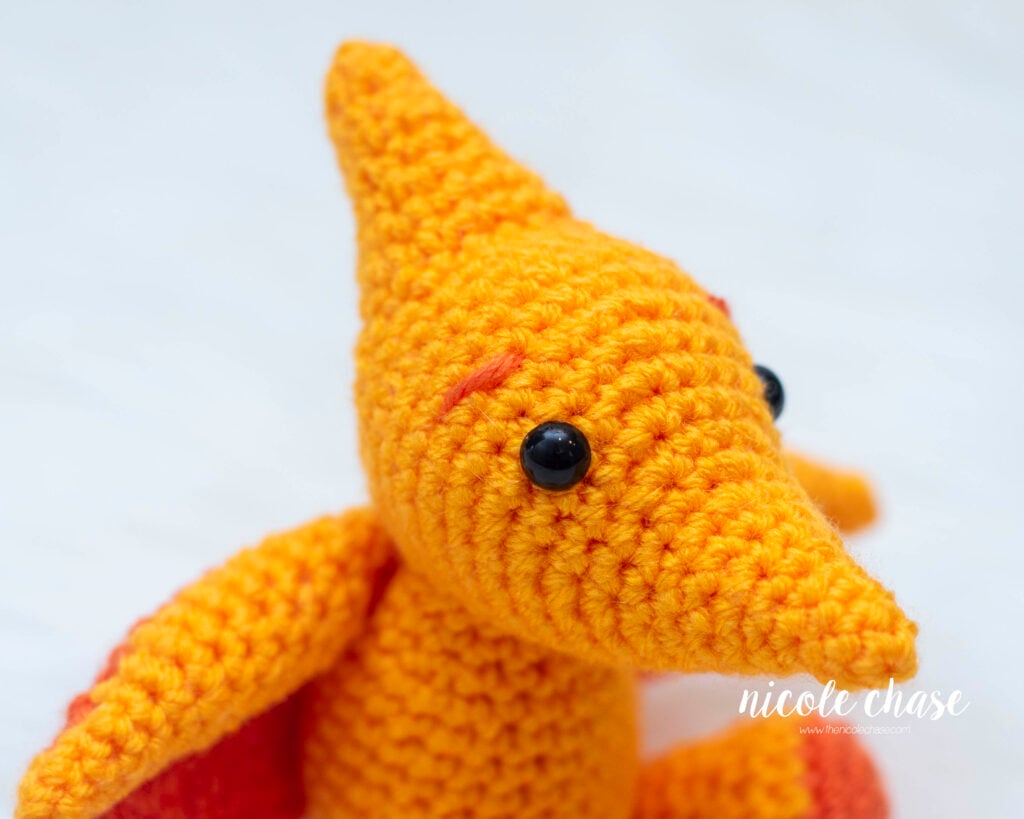 Close-up detail of the head, safety eye, and a stitched eyebrow on Mini Tori the Pterosaur, a free mini pterodactyl crochet pattern.