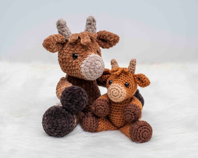 Two crochet highland cows made from the Hazel the Highland Cow crochet pattern by Nicole Chase. The one on the left is made in plush yarn and is larger, while the one on the right is made in worsted weight yarn and is smaller.