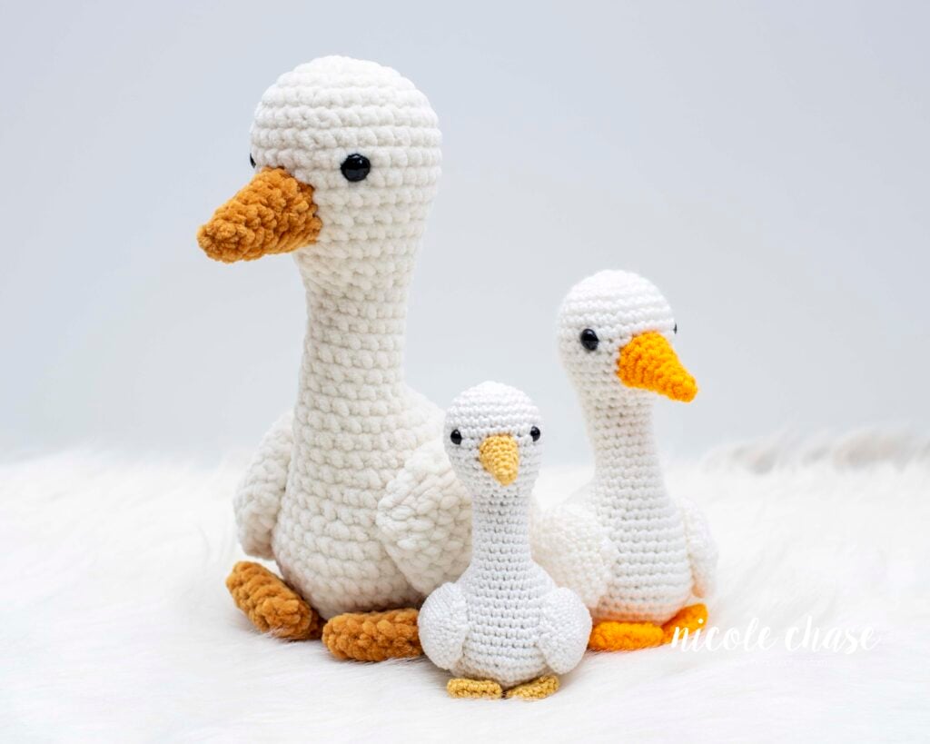 A family of three crochet goose amigurumi toys made using this free goose crochet pattern, showing the size differences between the large plush chenille version, the medium worsted weight version, and the small DK weight version.